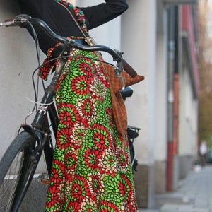 May include: A black bicycle with a vibrant floral skirt. The skirt displays a pattern of red and green flowers on a white base. The person is wearing a black top and a red hat.