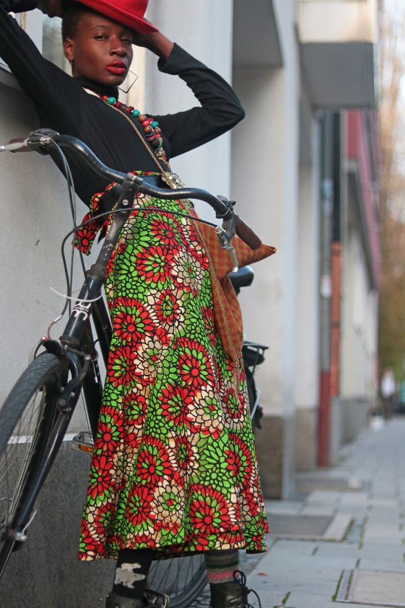 May include: A black bicycle with a vibrant floral skirt. The skirt displays a pattern of red and green flowers on a white base. The person is wearing a black top and a red hat.