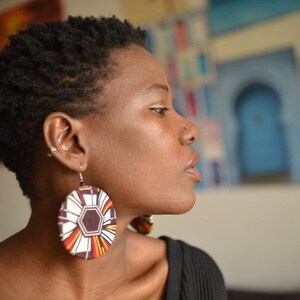 May include: A woman with short, dark hair wearing a black shirt and large, round earrings with a colorful geometric pattern.