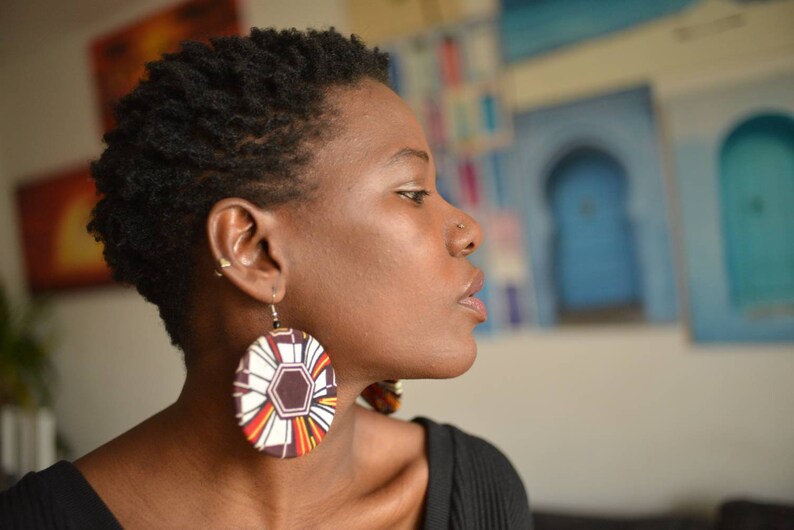 May include: A woman with short, dark hair wearing a black shirt and large, round earrings with a colorful geometric pattern.