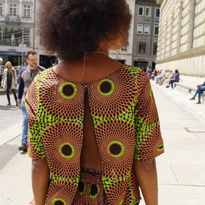 May include: A patterned two-piece outfit featuring a top with a back cutout and matching shorts. The fabric has a brown background with green and brown circular designs. The person is facing away from the camera.