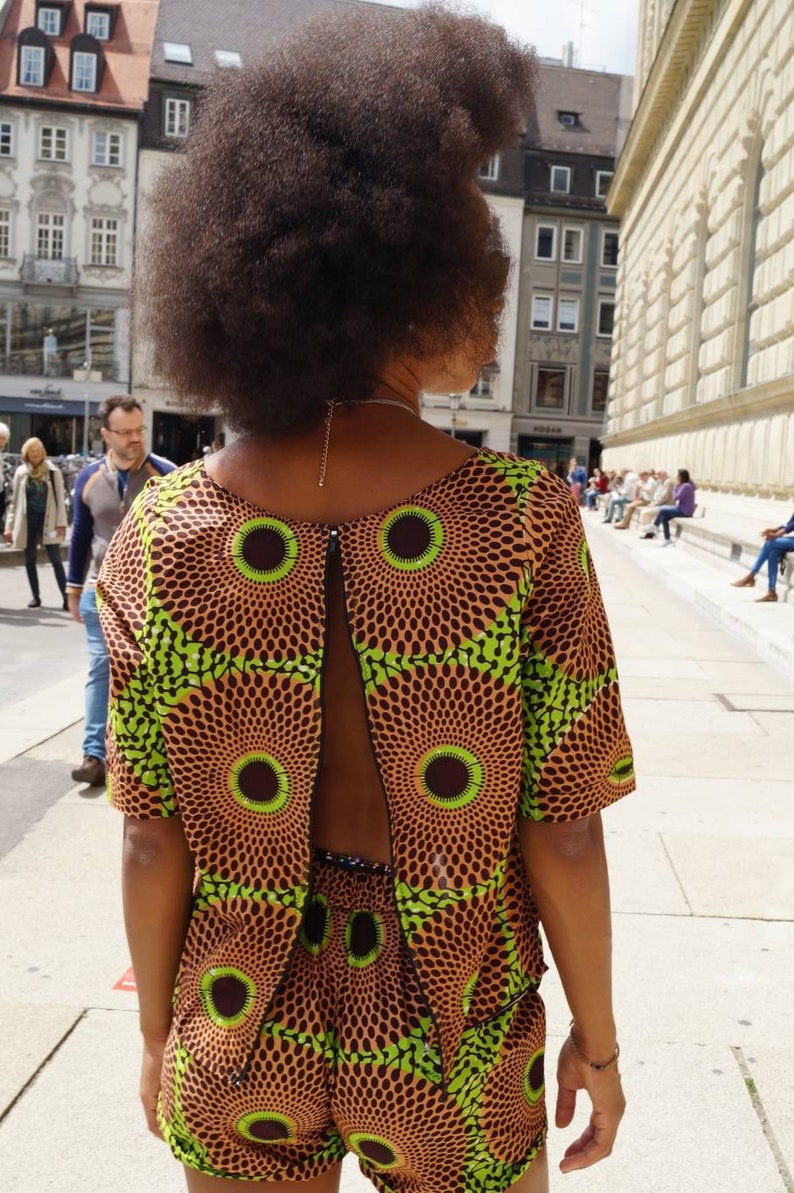 May include: A patterned two-piece outfit featuring a top with a back cutout and matching shorts. The fabric has a brown background with green and brown circular designs. The person is facing away from the camera.