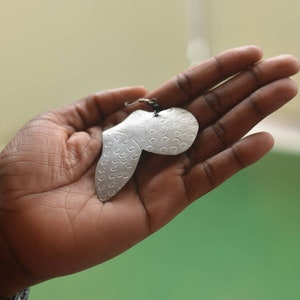 May include: A silver earring with a unique, textured design. The earring is shaped like a heart with a small loop at the top for attaching to a hook.
