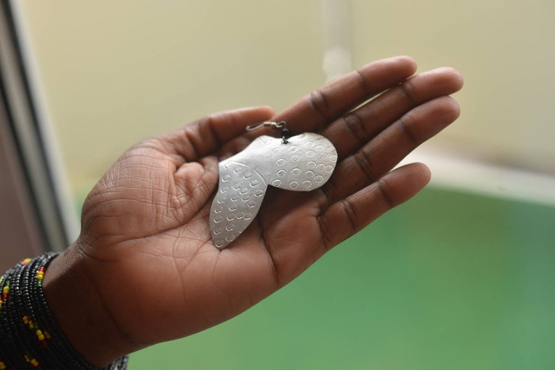 May include: A silver earring with a unique, textured design. The earring is shaped like a heart with a small loop at the top for attaching to a hook.