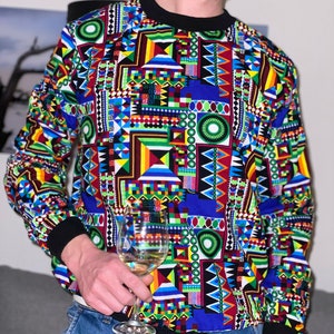 May include: A long-sleeved shirt with a striking geometric pattern in multiple colours, including blue, red, yellow, and green, and black collar and cuffs. The person is holding a clear wine glass with white wine.