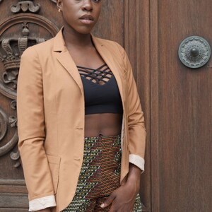 May include: A tan blazer with a black top and patterned shorts. The blazer has a classic design with a notched lapel and button closure. The shorts feature a colorful geometric pattern. The background is a wooden door.
