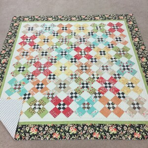 May include: A patchwork quilt with a green, white, and black checkered pattern. The quilt has a floral border in black, white, and pink.