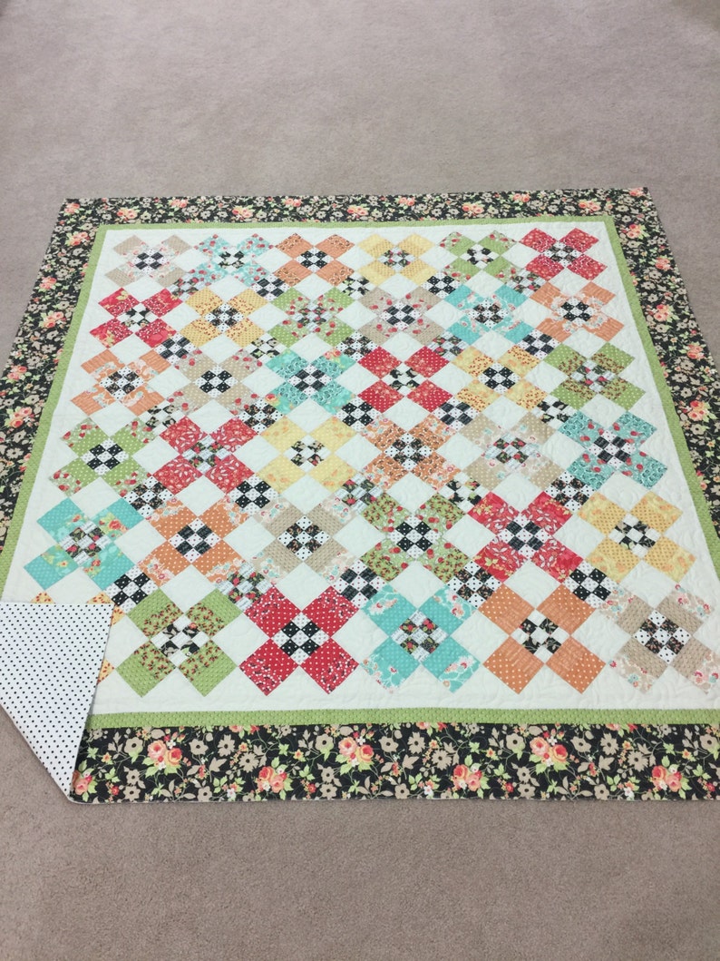 May include: A patchwork quilt with a green, white, and black checkered pattern. The quilt has a floral border in black, white, and pink.