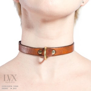 Pode incluir: Um colar de couro marrom com um anel de metal dourado.  LVX Supply & Co.  Cor do couro: Marrom claro.  Hardware: Lat&atilde;o.