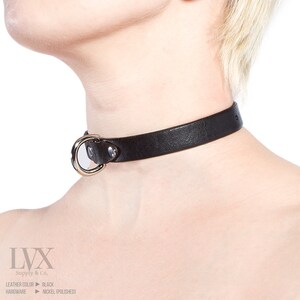Pode incluir: Um colar de couro preto com um anel prateado e dois tachas prateadas. O colar &eacute; feito por LVX Supply & Co. e o hardware &eacute; de n&iacute;quel polido.
