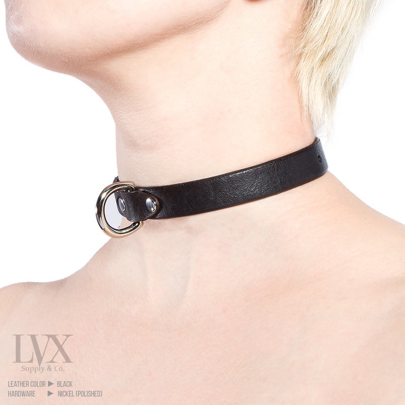 Pode incluir: Um colar de couro preto com um anel prateado e dois tachas prateadas. O colar &eacute; feito por LVX Supply & Co. e o hardware &eacute; de n&iacute;quel polido.