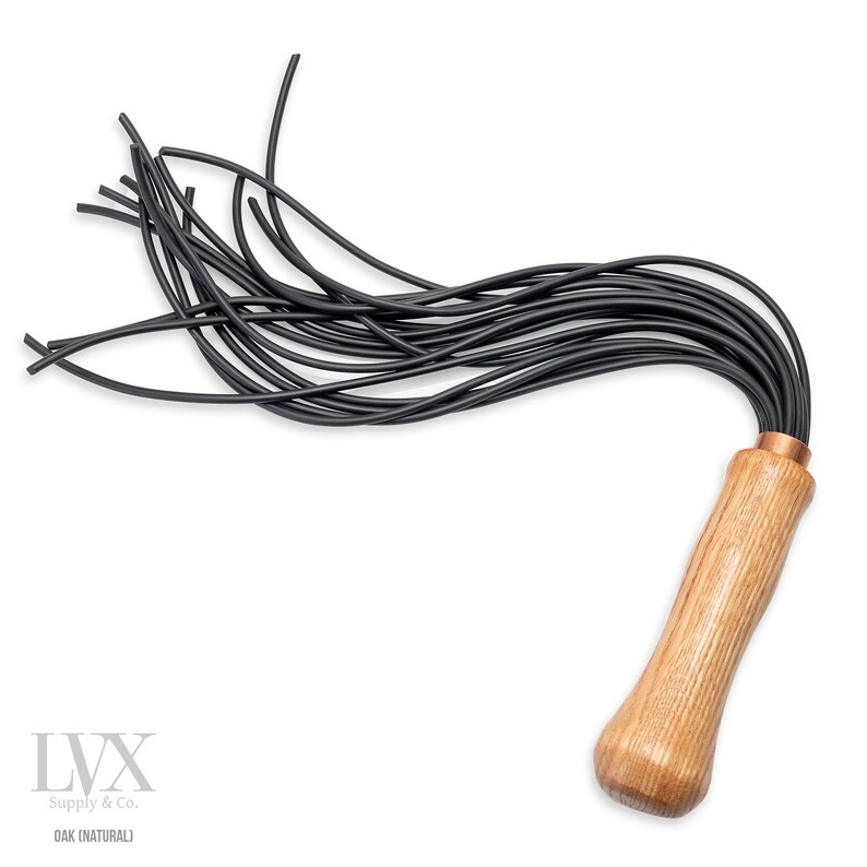 May include: A black leather whip with a wooden handle. The handle is made of natural oak wood and has a copper accent at the top. The whip has multiple strands of leather that are tied together at the handle.