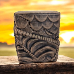 May include: A dark brown wooden box with a detailed, intricate design. The box has a hinged lid and a textured surface.