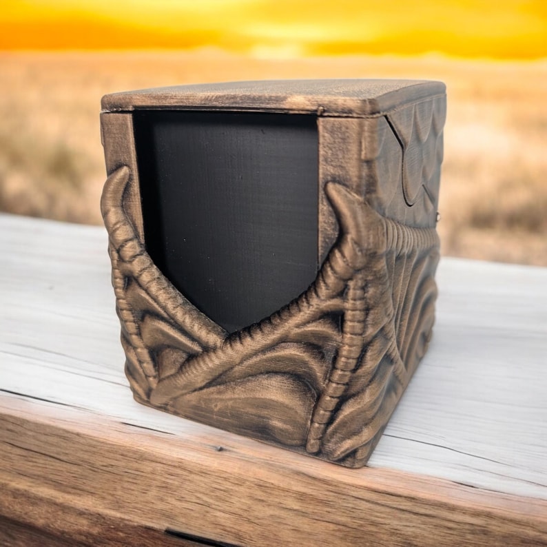 May include: A gold-colored wooden box with a dragon design. The box has a hinged lid and a black interior.