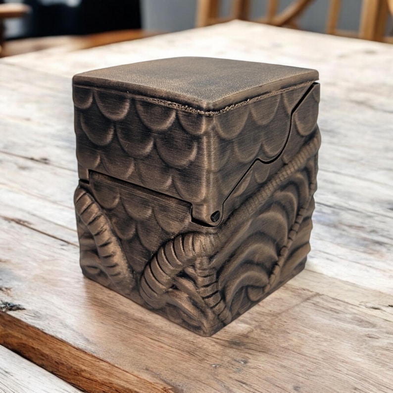 May include: A small, intricately carved wooden box with a bronze finish. The box has a hinged lid and a decorative design of scales and swirling patterns.