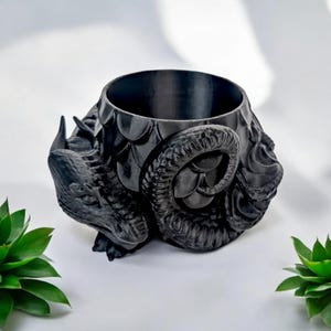 Pode incluir: Um vaso de plantas preto com tema de drag&atilde;o com um design detalhado e texturizado. O vaso apresenta uma abertura ampla e &eacute; adornado com escamas e chifres de drag&atilde;o. A cabe&ccedil;a e os chifres enrolados do drag&atilde;o s&atilde;o caracter&iacute;sticas proeminentes.