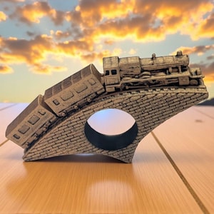 May include: A detailed, gray miniature train and passenger car are depicted on a brick bridge. The bridge has a circular opening. The background features a sunset with orange and yellow hues. The train is a decorative item.