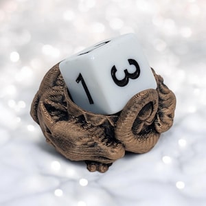 May include: A bronze-colored dragon figurine holding a white six-sided die with the number "3" facing up.