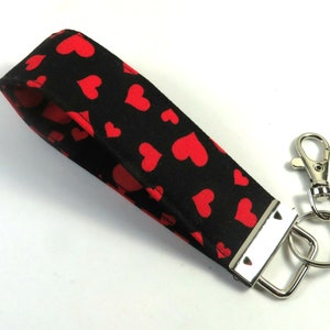 May include: A black and red key chain with a red heart pattern. The key chain has a silver metal ring and a silver metal clip.