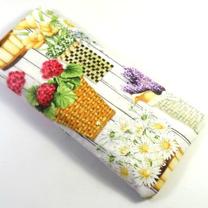Op de afbeelding: Een wit stoffen brilletje met een bloemenprint met gele, witte, roze en paarse bloemen in rieten manden. De achtergrond is een wit houtnerfpatroon.