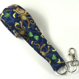 May include: A blue fabric lanyard with a monkey and banana pattern. The lanyard has a silver key ring and a silver clip.