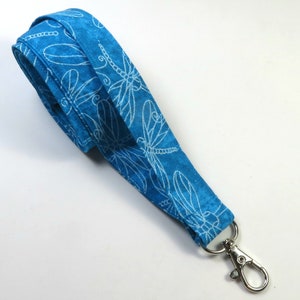May include: A blue fabric lanyard with a white dragonfly pattern and a silver swivel clip.