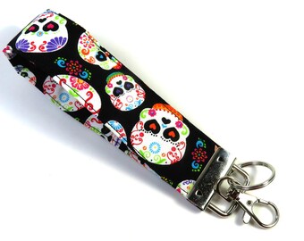 May include: A black key chain with a colorful sugar skull pattern. The key chain has a silver metal clasp and a silver ring.