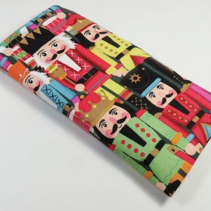 May include: A colorful fabric with a repeating pattern of nutcracker soldiers. The nutcrackers are wearing red, blue, green, and yellow uniforms with gold accents. The fabric has a white background.