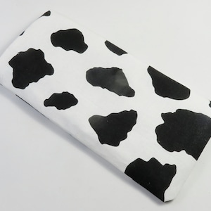 Può includere: Un tessuto rettangolare bianco con un motivo di stampa di mucca nera.