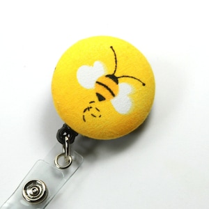 May include: A yellow retractable badge holder with a cartoon bee design. The bee is black and white with yellow stripes.