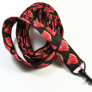 May include: A black lanyard with a repeating pattern of red watermelon slices. The lanyard has a black metal swivel clasp. The fabric is a cotton blend. The lanyard is approximately 36 inches long.