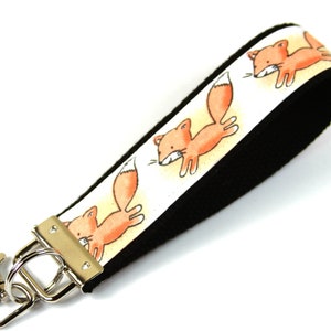 May include: A white and black key chain with a repeating pattern of orange foxes. The key chain has a silver metal clasp.
