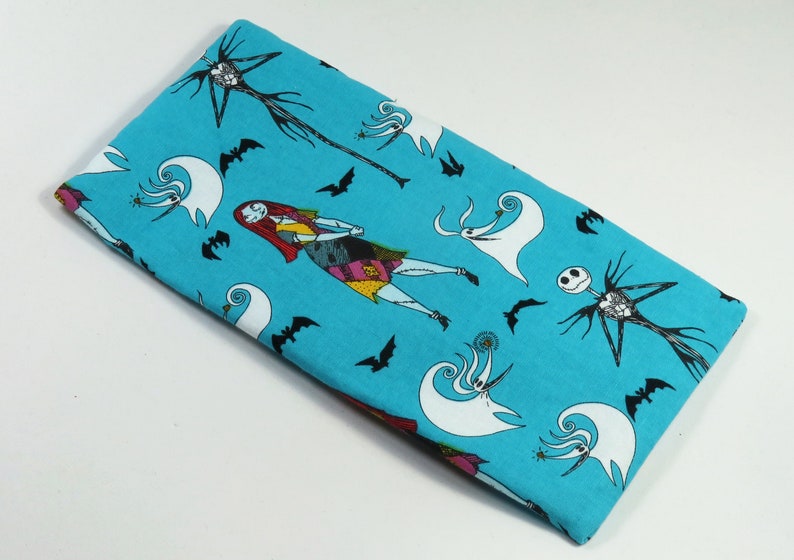 May include: A turquoise fabric with a repeating pattern of characters from The Nightmare Before Christmas. The characters include Jack Skellington, Sally, and Zero the ghost dog.