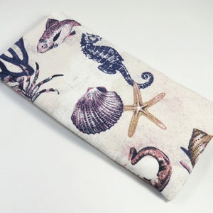May include: A white fabric eye mask with a sea life print. The print features a seahorse, starfish, seashells, and a crab.