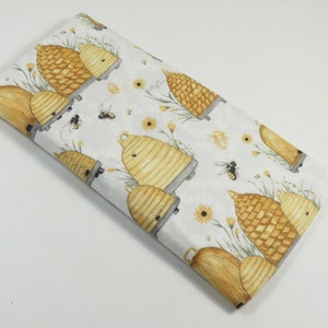 May include: White fabric with a repeating pattern of yellow and brown beehives, yellow flowers, and small black bees.