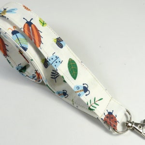May include: White fabric lanyard with a colorful bug and leaf pattern and a silver swivel clasp.