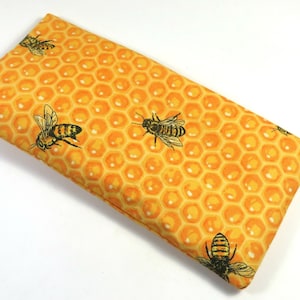 May include: A yellow fabric pouch with a honeycomb pattern and black and yellow bees. The pouch is made of a soft, durable fabric and is perfect for storing small items.