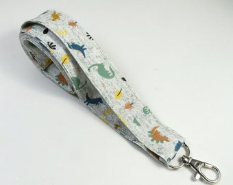 May include: A white fabric lanyard with a dinosaur print and a silver swivel clip. The lanyard is approximately 1.5 inches wide.