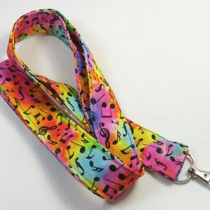 May include: A colorful lanyard with a tie-dye pattern and black musical notes. The lanyard has a silver swivel clip.