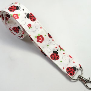 May include: White lanyard with a red and black ladybug pattern. The lanyard has a silver swivel clasp.