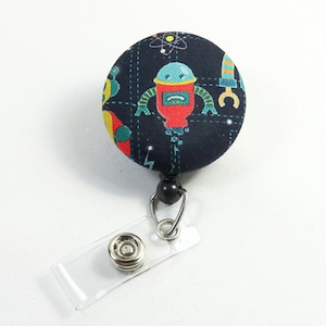 May include: A black retractable badge holder with a round fabric button featuring a colorful robot design. The button has a black and white background with a repeating pattern of robots, stars, and lightning bolts.