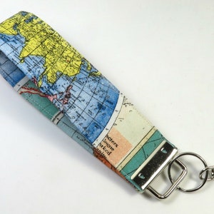 May include: A blue and yellow world map key chain with a silver key ring. The map is printed on a fabric strap.