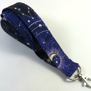 Könnte beinhalten: Ein dunkelblaues Lanyard mit einem weißen zellischen Druck mit Sternen, Monden und Sternbildern. Das Lanyard hat einen silbernen Metall-Drehverschluss.
