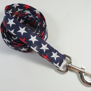 May include: A blue and white dog leash with red stars. The leash has a silver clip.
