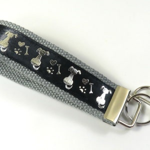 May include: A gray and black key chain with a silver key ring and a black ribbon with silver paw prints and dog silhouettes. The ribbon says "I love dogs".