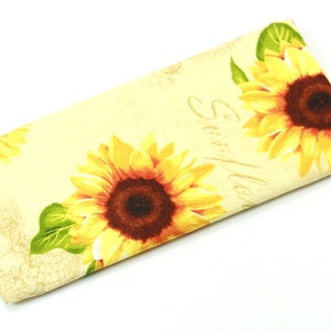 Puede incluir: Un estuche para gafas de color crema con estampado de girasoles y el texto "Sunflower" en letra cursiva.