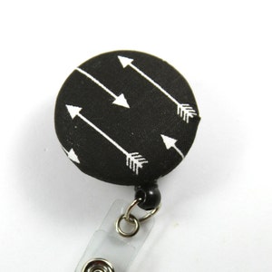 May include: Black retractable badge holder with a white arrow pattern on the button.