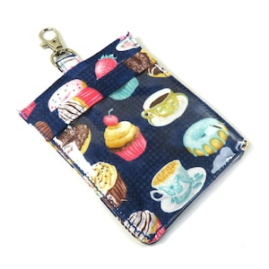 May include: A blue fabric key chain with a clear plastic window. The fabric has a pattern of cupcakes, donuts, and teacups. The key chain has a silver metal clip.