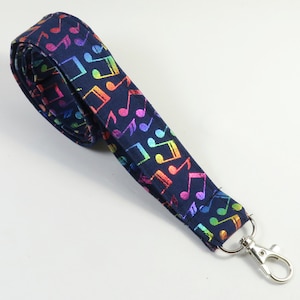 May include: A navy blue lanyard with a rainbow musical note pattern and a silver swivel clip.