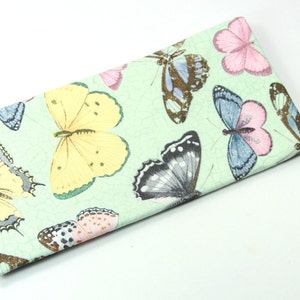 May include: A green fabric eyeglass case with a butterfly print. The butterflies are in various colors, including yellow, pink, blue, and black.